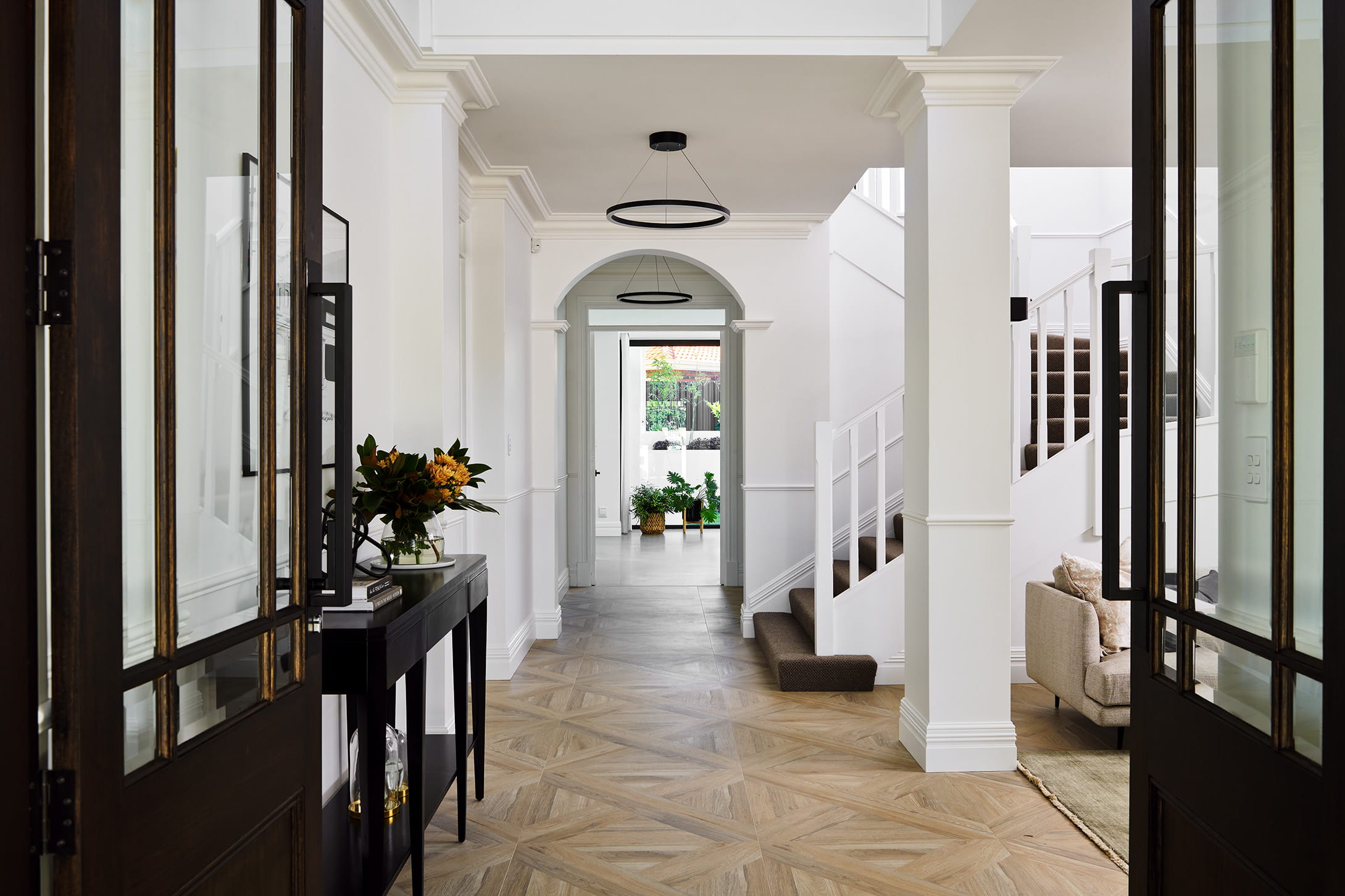 Grand entry hallway in a custom Perth home with decorative columns, arched doorway, parquetry timber flooring and ring pendant lights.