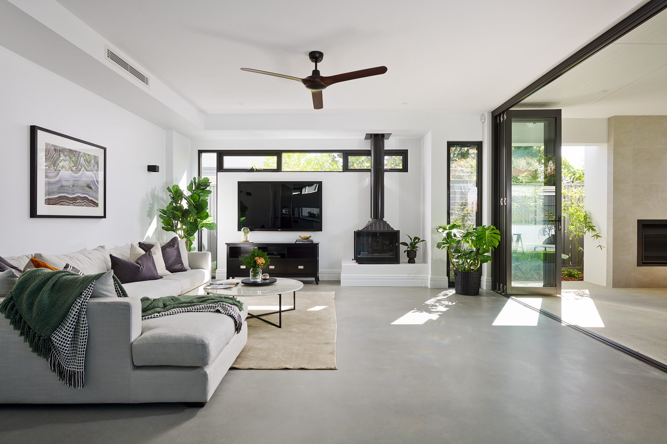 Contemporary living room in a custom Perth home with polished concrete floors, freestanding black fireplace and black-framed stacker doors opening to the alfresco.