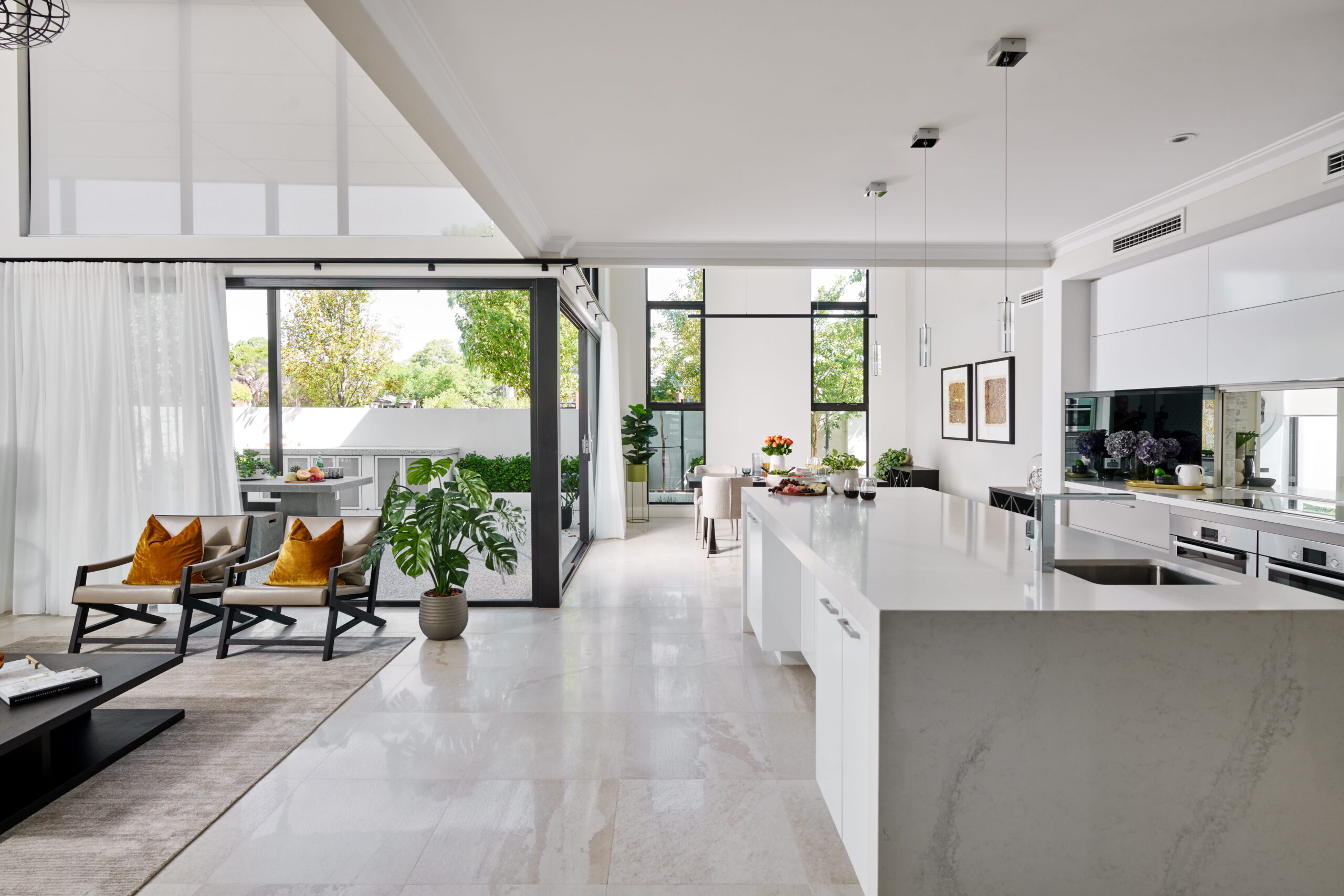 Open-plan kitchen and living area in a custom Perth home with stone island bench, large-format floor tiles and floor-to-ceiling black-framed windows.