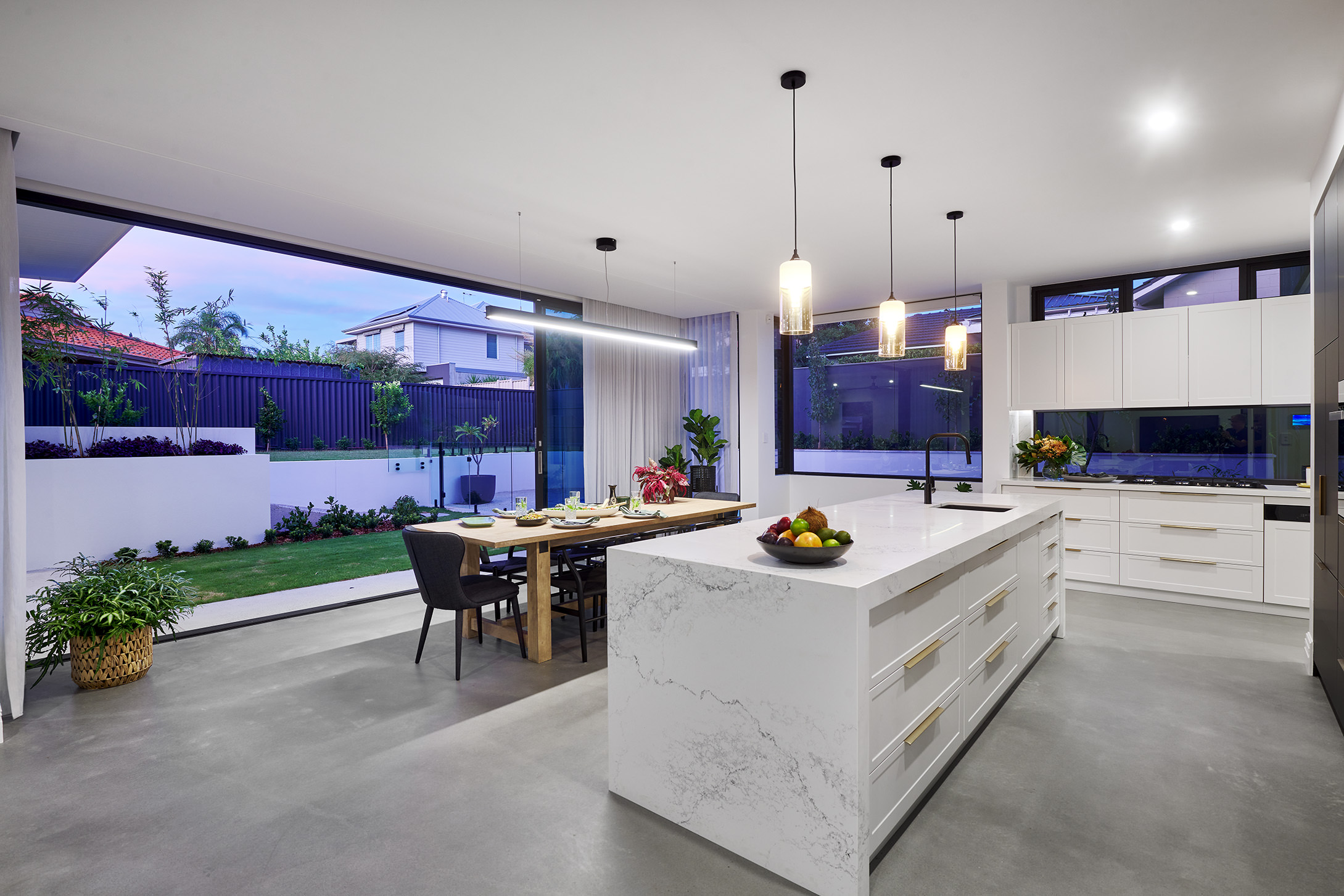 Luxury kitchen in a custom Perth home with marble stone island, polished concrete floors and fully opened stacker doors to the alfresco at dusk.