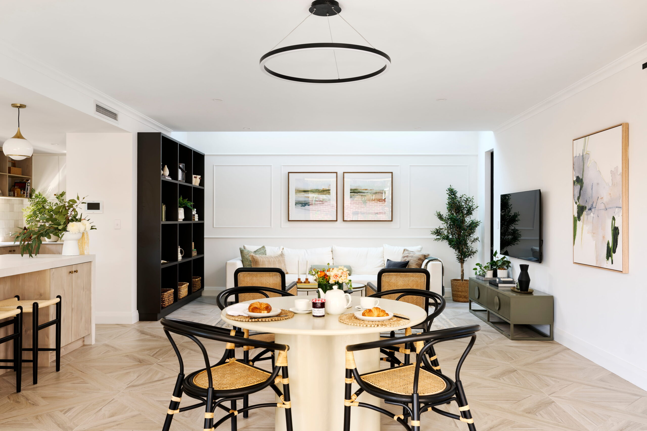 Open-plan dining and living area in a custom Perth home with parquetry floors, round dining table, rattan chairs and panelled feature wall.