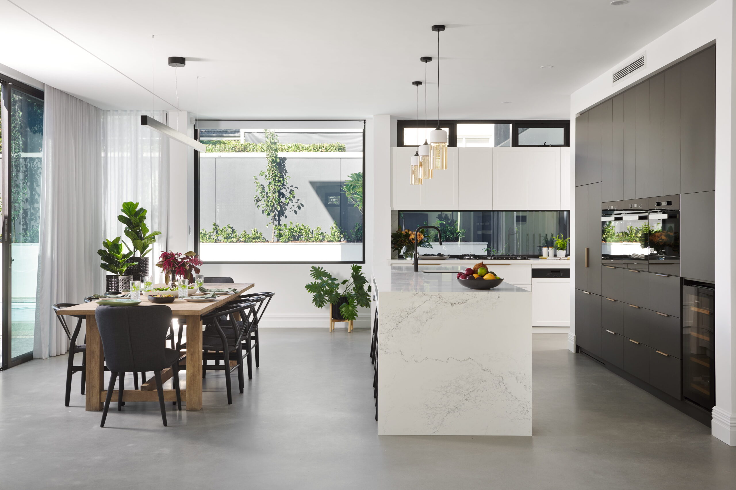 Open-plan living, dining and kitchen in a custom Perth home with polished concrete floors, marble island bench and glass doors to the garden.