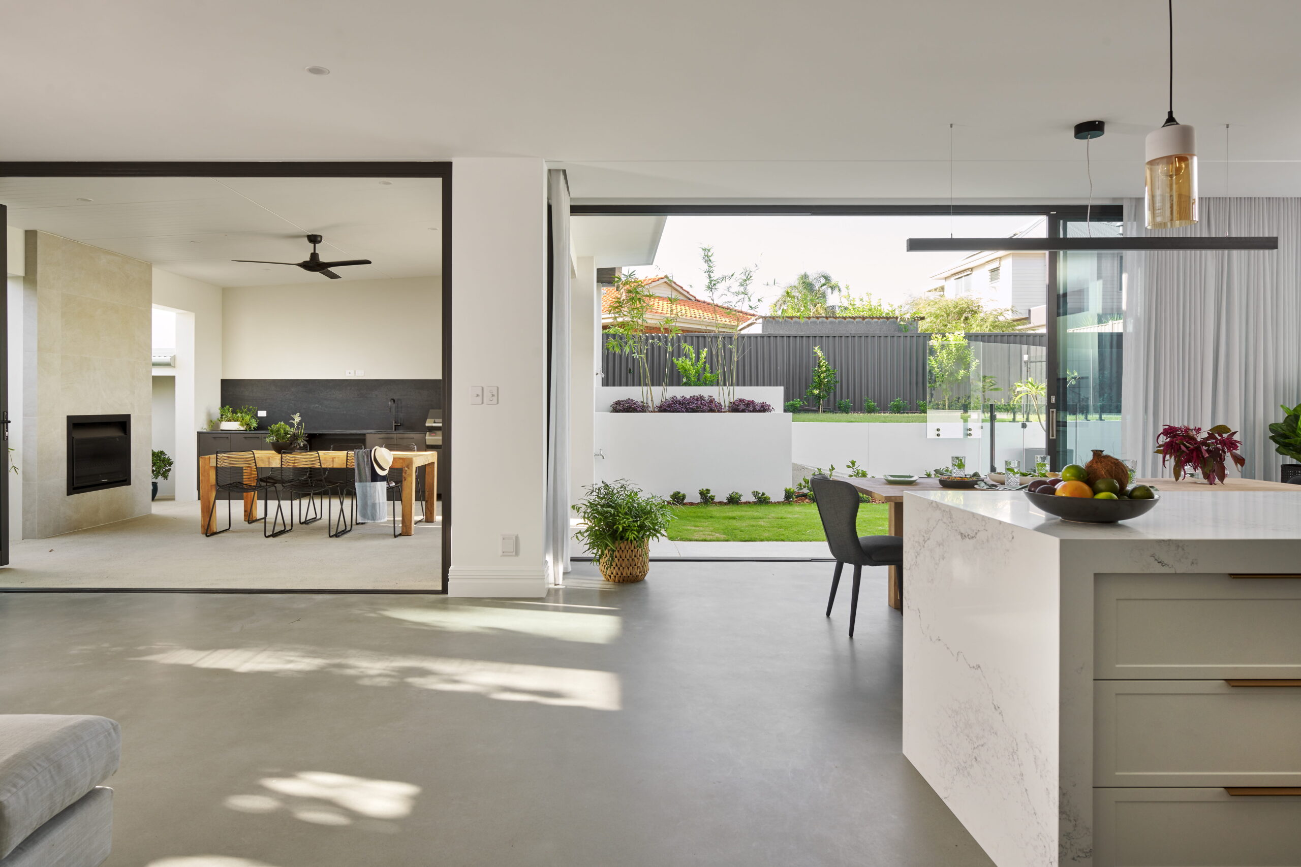 Open-plan living, dining and kitchen in a custom Perth home with polished concrete floors, marble island bench and glass doors to the garden.