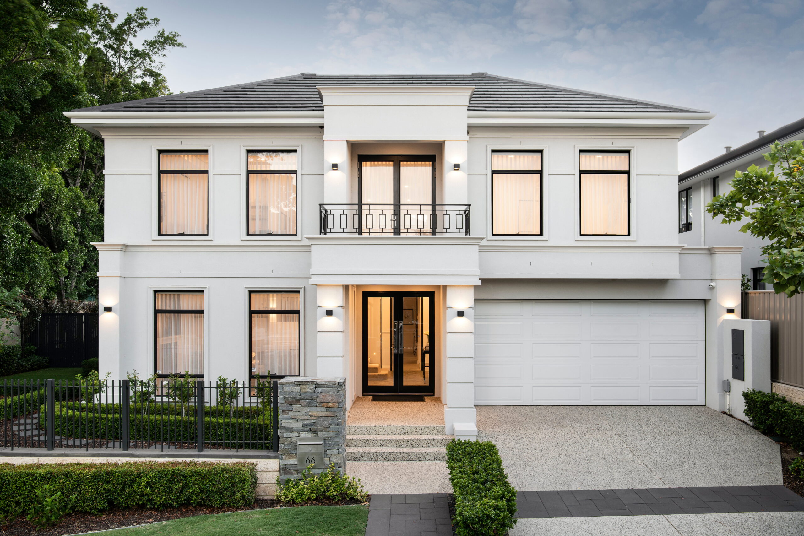Two-storey luxury custom home built by Stannard Homes in Perth, with French contemporary facade with white render, wrought-iron balcony, stone pillar detailing and formal landscaped frontage