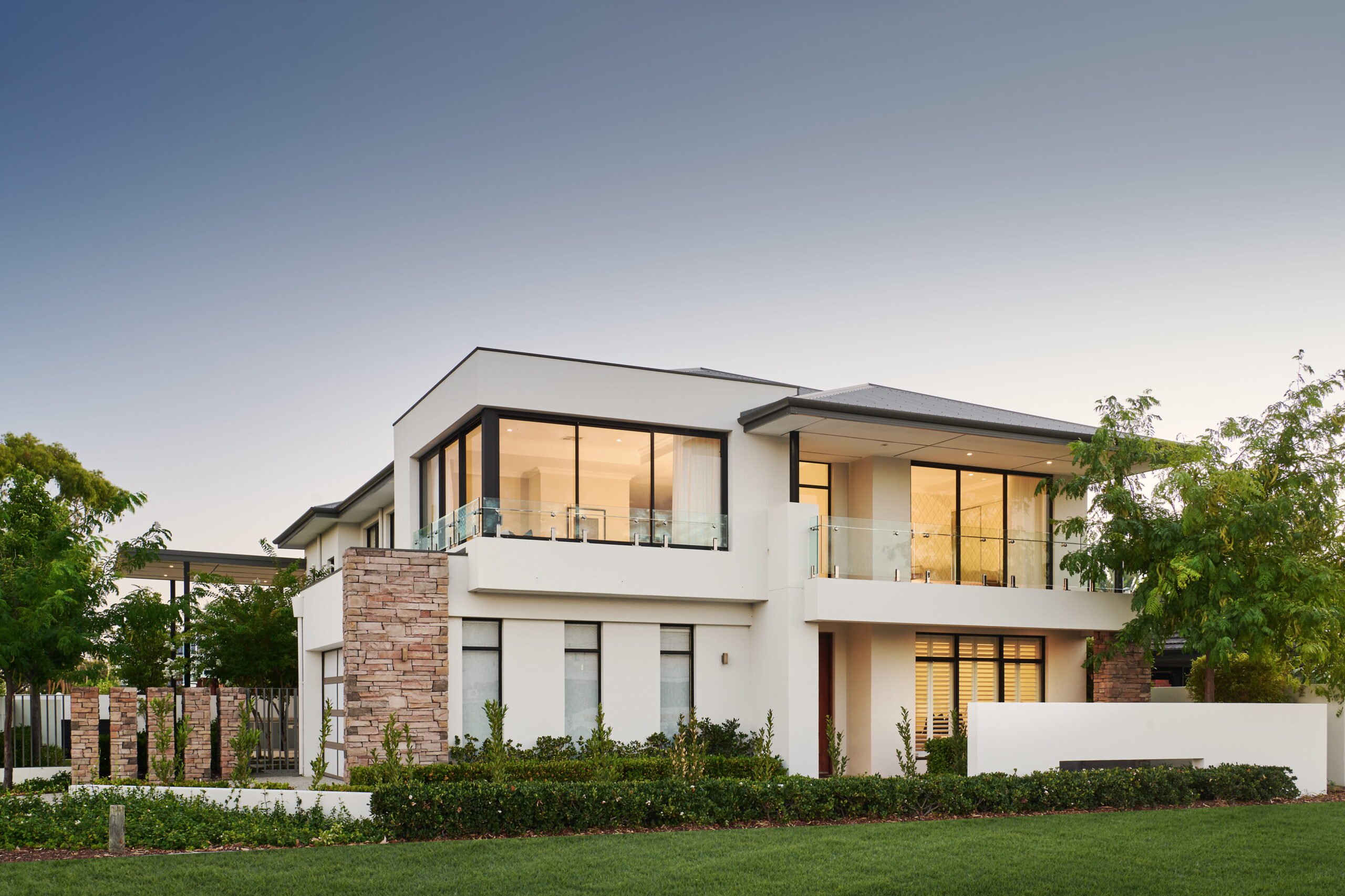 Two-storey contemporary custom home built by Stannard Homes in Perth, with a stone facade with floor-to-ceiling glazing, glass balustrades and a manicured garden.