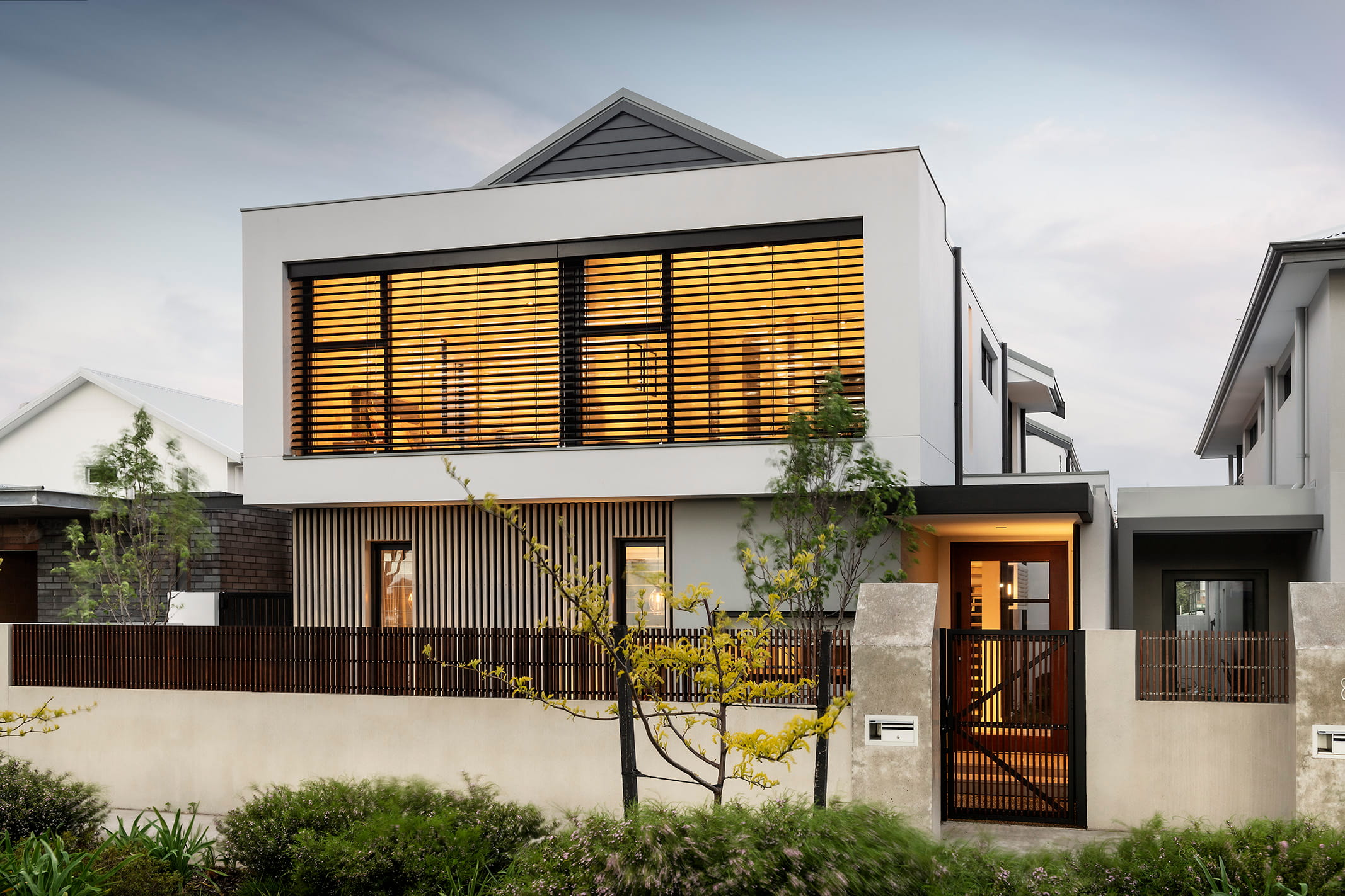 Exterior of a modern two-story luxury home in Perth at dusk, featuring warm interior lighting and vertical timber slats.